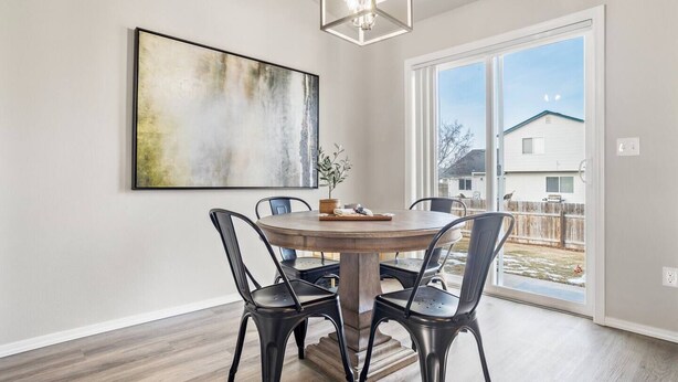 Een eetgedeelte met een ronde tafel, vier stoelen, een groot abstract schilderij en uitzicht op een huis door een glazen deur.