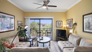 A living room with a ceiling fan, a TV, and a balcony with chairs and a table. - Cozy Desert Getaway*Inviting Pool*Smart TV*Gym (Fountain Hills)