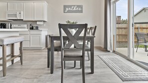 A modern kitchen with white cabinets, a dining area with a dark wooden table and chairs, and a 'gather' sign on the wall. - *FirePit*King*Parking*1600ft²*Smart TV*W/D (Meridian)
