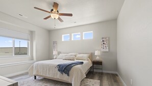 Une chambre à coucher avec un lit, un ventilateur de plafond, une fenêtre et une table de chevet avec une lampe.