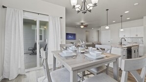 Un espace repas moderne avec une table en bois pour quatre personnes, un ventilateur de plafond et des luminaires suspendus.