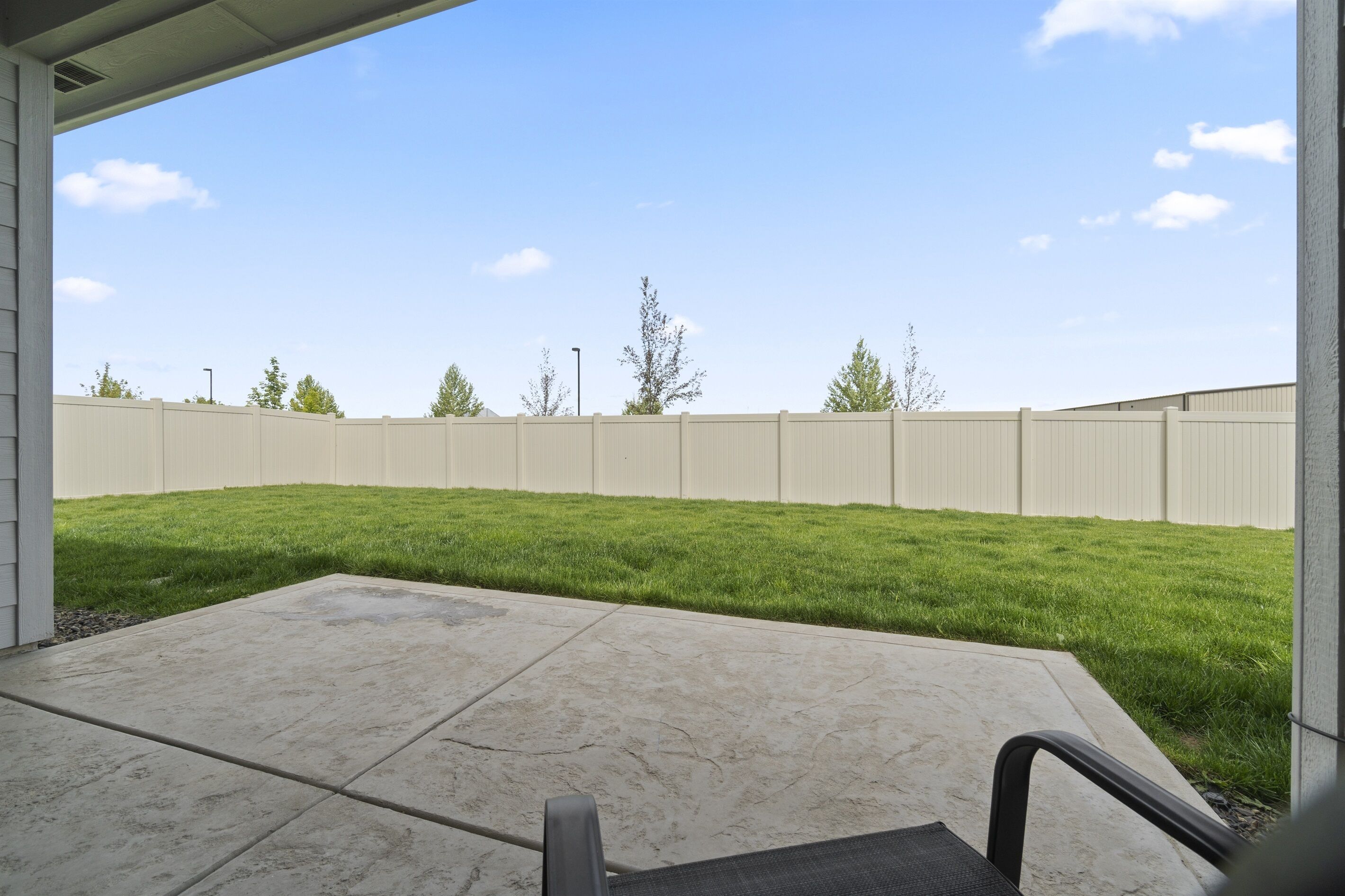A patio with a concrete floor and a view of a fenced yard with grass and trees.