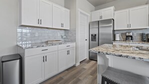 Une cuisine moderne avec des meubles blancs, un réfrigérateur en acier inoxydable et un plan de travail en marbre.
