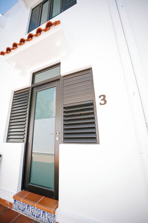 A white building with a glass door, a number '3' on the wall, and a tiled entrance.