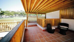 Un espace extérieur abrité, doté de rampes en bois, de deux fauteuils en osier et d’un sol carrelé.
