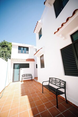 A white building with a tiled patio, a bench, and a door.