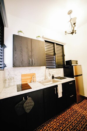 A kitchen with a marble countertop, a sink, a stove, black cabinets, and a refrigerator.