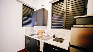A compact kitchen with dark cabinets, a stainless steel refrigerator, a microwave, and a sink with a marble countertop. - Original Spanish Architecture in the Heart of SanJuan w/Parking (San Juan)