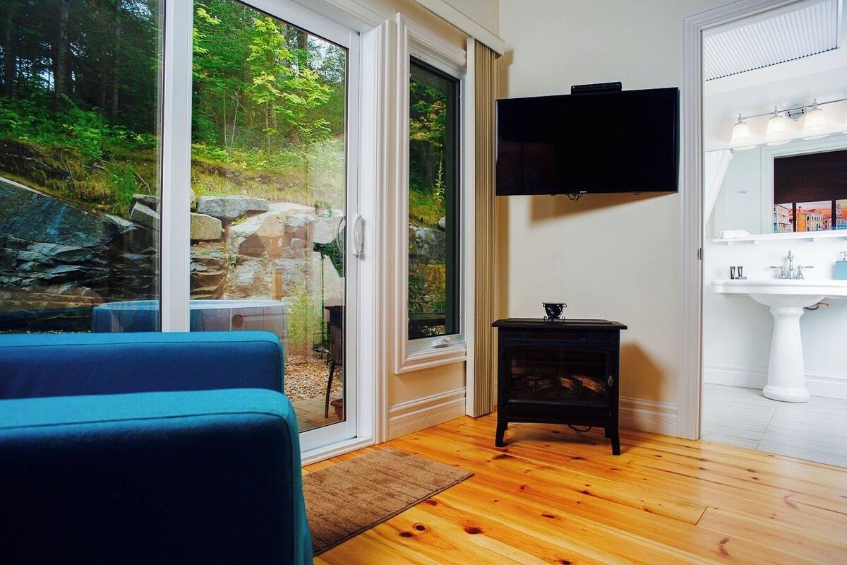 A room with a large sliding glass door leading to a stone garden, a black TV mounted on the wall, and a white sink in the corner.