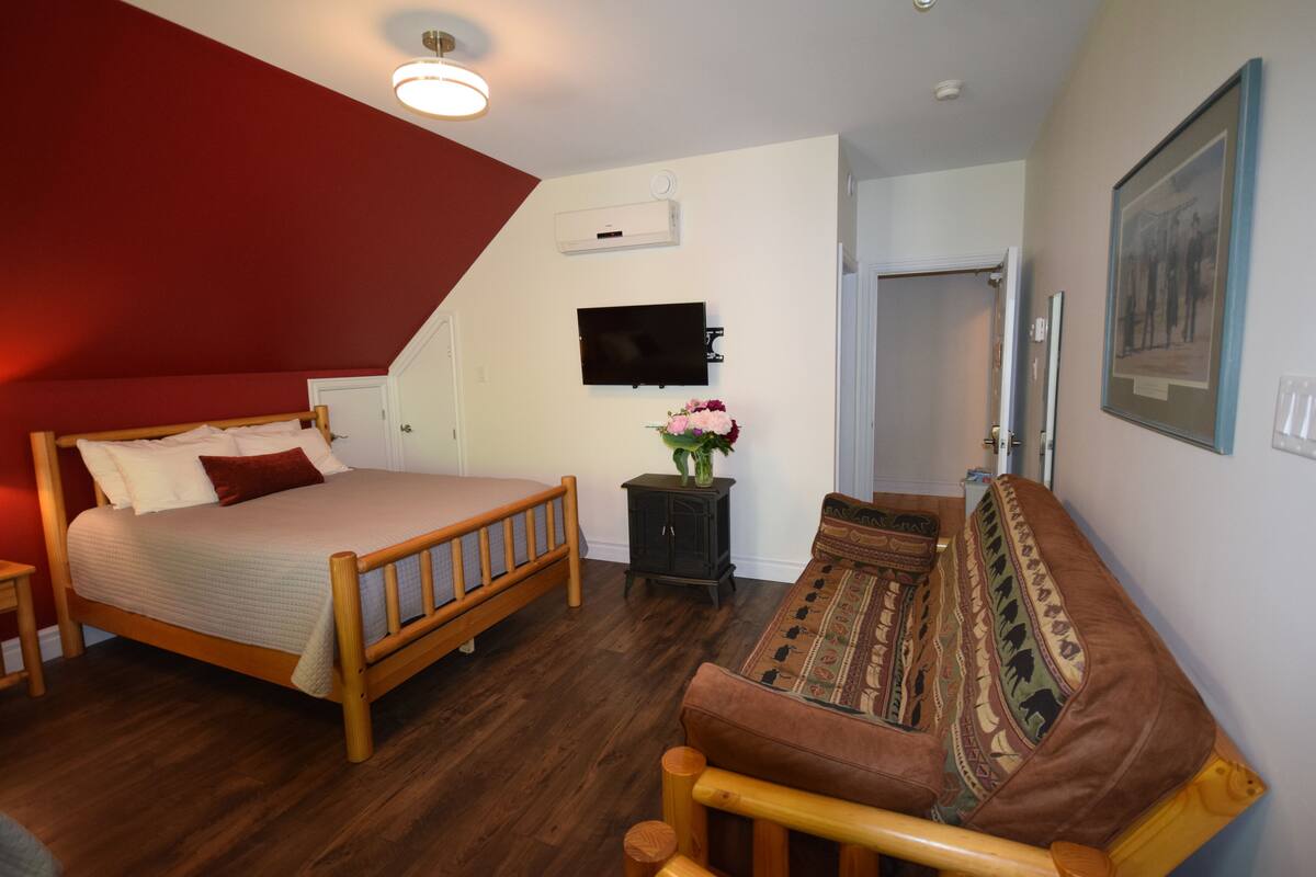 A bedroom with a wooden bed, a sofa, a TV, and a small cabinet with a vase of flowers.