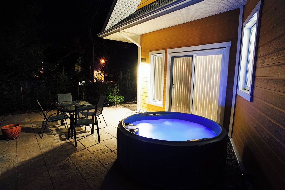 A hot tub in a backyard with a table and chairs, a wooden fence, and a sliding glass door.