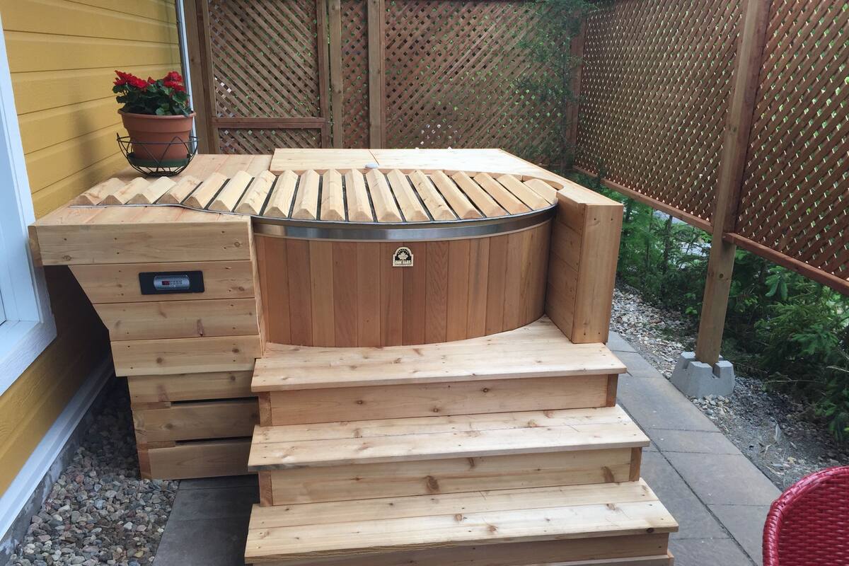 A wooden outdoor hot tub with steps leading up to it, a control panel, and a potted plant nearby.