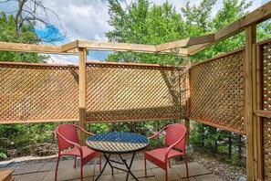 A covered patio area with a round table and two red chairs, surrounded by wooden lattice panels. - Belle de Nuit (La Peche)