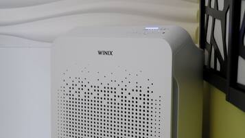A white air purifier with the brand name WINIX, placed on a wooden floor against a wall with a geometric pattern.
