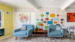 Ein modernes Wohnzimmer mit zwei blauen Sesseln, einem Couchtisch und abstrakter Wandkunst.