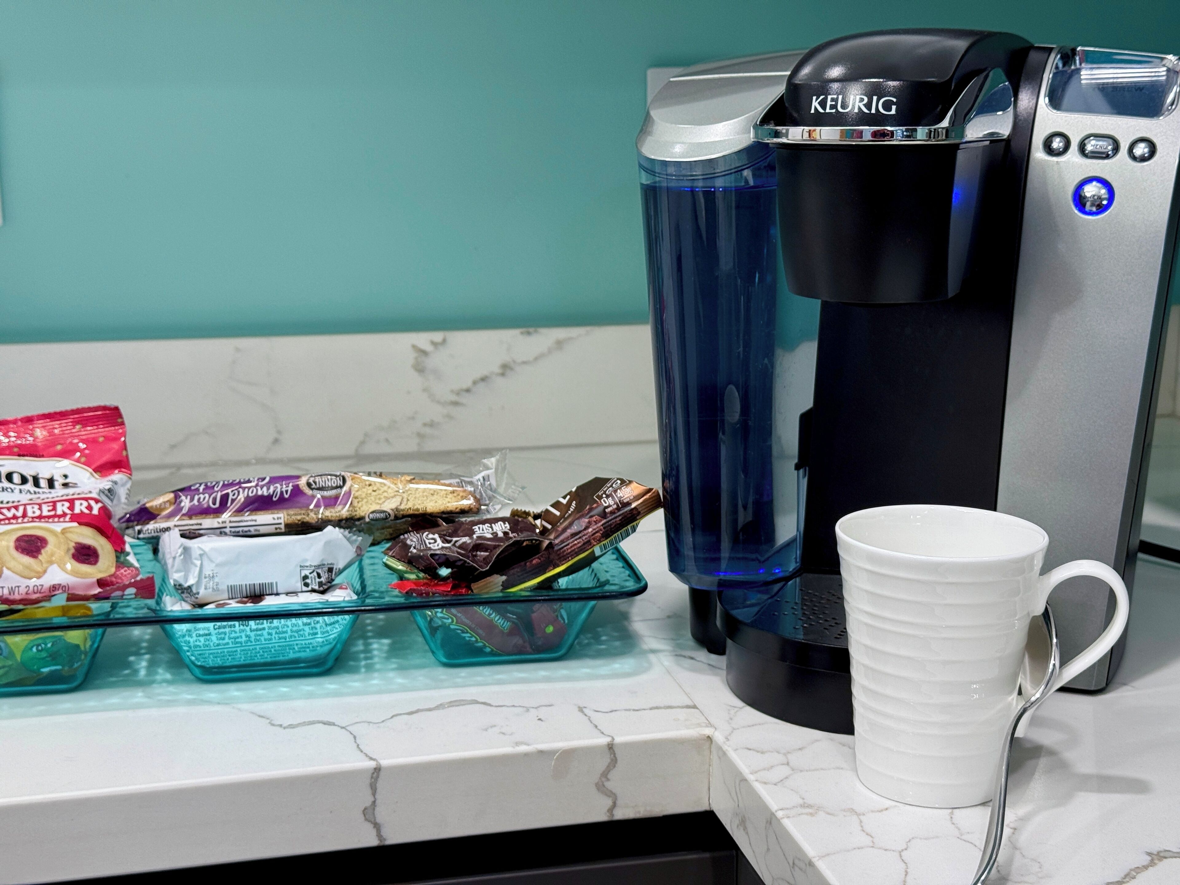 Une machine à café, une tasse blanche et des boîtes à collation sur un plan de travail de cuisine.