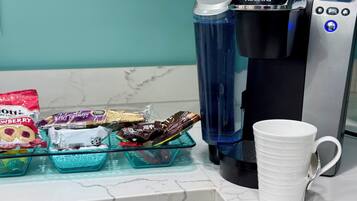 Une machine à café, une tasse blanche et des boîtes à collation sur un plan de travail de cuisine.