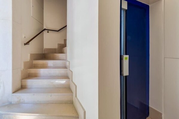 A staircase with a handrail leading to a door with a blue frame and a control panel. - Setúbal Prime Penthouse (Setúbal)