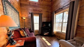 Interior acogedor de una cabaña con paredes de madera, chimenea, sofá y una mesa con lámpara.