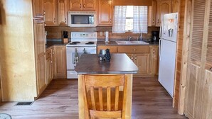 Una cocina tipo cabaña de madera con una isla central, armarios de madera, un microondas, estufa, fregadero y refrigerador.