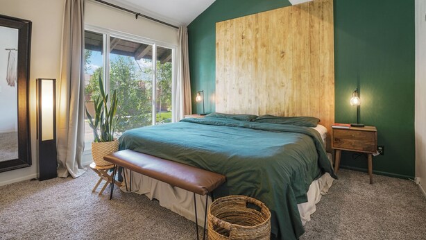 A bedroom with a large bed, a bench, a bedside table, a lamp, a window with curtains, and a view of greenery outside. - Cozy and modern townhome in Aurora, 5min from highway ! (Aurora)