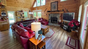 Interior acollidor d'una cabana amb una llar de foc, una televisió i un sofà de cuir vermell.
