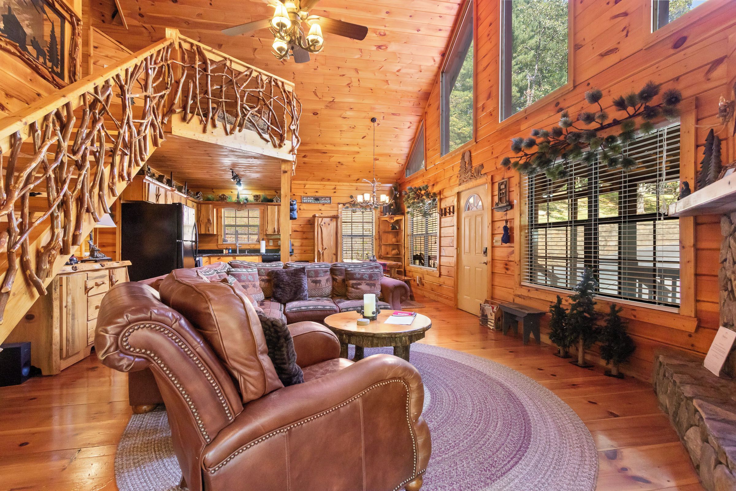 A log cabin interior with a large wooden staircase, a cozy seating area, and a fireplace.