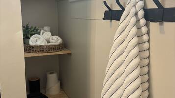 Une salle de bain équipée d’un porte-serviettes, d’étagères avec des serviettes pliées, d’un panier contenant des serviettes roulées et d’un rouleau de papier toilette.