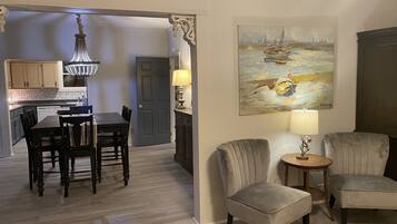 A dining area with a chandelier, a painting of a boat on water, and a door leading to a kitchen.