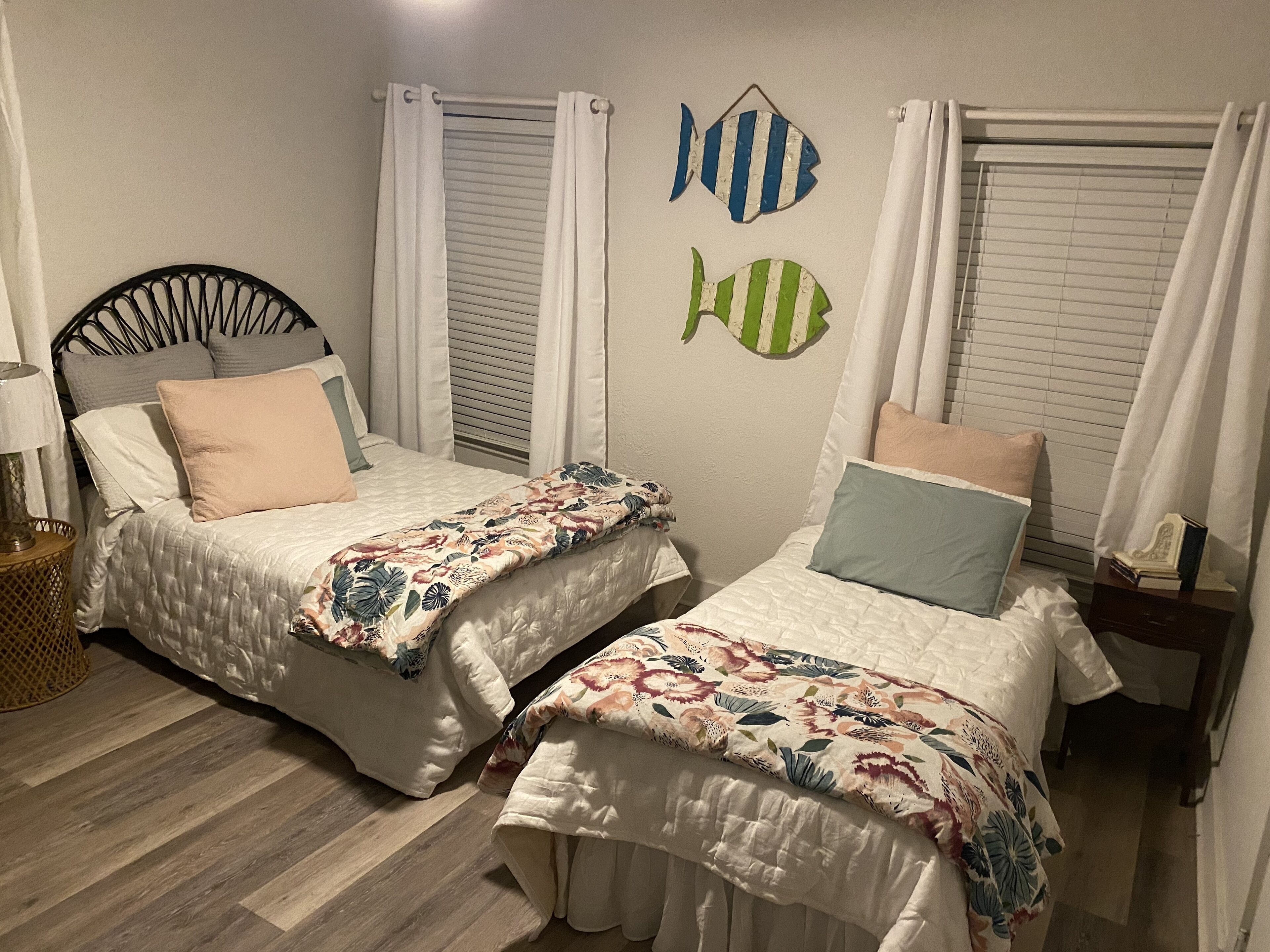 A bedroom with two beds, white curtains, and decorative fish wall art.