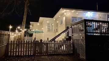 A two-story house with a white exterior, a wooden deck, and a staircase leading to the upper floor.