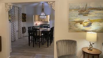 A dining area with a table and chairs, a chandelier, and a painting of a seascape.