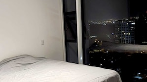 A bedroom with a bed, a sliding glass door leading to a balcony with a city view at night. - Luxurious apartment one block from the National Stadium (San José)