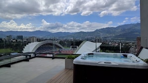 A rooftop terrace with a hot tub, a view of mountains, and a stadium in the background. - Luxurious apartment one block from the National Stadium (San José)