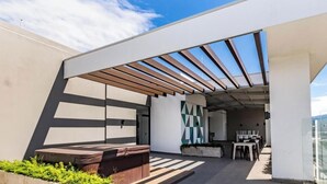 A modern outdoor terrace with a wooden pergola, seating area, and a view of the city. - Luxurious apartment one block from the National Stadium (San José)