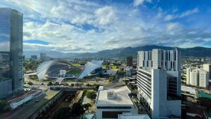 A cityscape with modern buildings, a stadium, and a mountain range in the background. - Luxurious apartment one block from the National Stadium (San José)