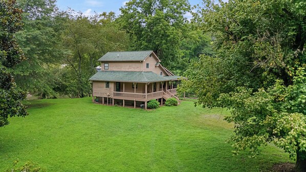 Kaksikerroksinen puutalo, jossa on kuisti, ja sen ympärillä on hyvin hoidettu nurmikko ja tiheä puusto.