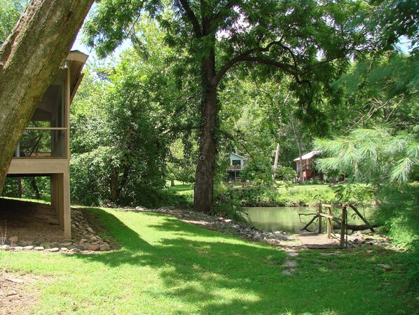 A wooden cabin with a deck, surrounded by lush greenery and a pond.