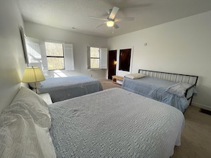 A bedroom with two beds, a ceiling fan, and a window with a view of trees.