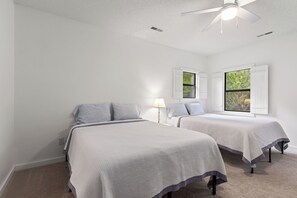 A bedroom with two beds, a ceiling fan, and windows with shutters.