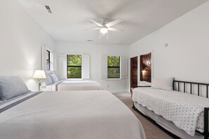A bedroom with two beds, a ceiling fan, and windows with shutters.