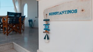 A sign with the name "KONSTANTINOS" on a white wall, a wooden chair, and a table in the background. - Cycladic Seaside House “Konstantinos” by Kastraki Family House (Kastraki Naxos)