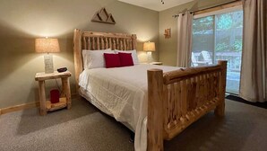 Quarto com cama de madeira, duas luminárias de cabeceira, um ventilador de teto e vista para o exterior por uma grande janela.