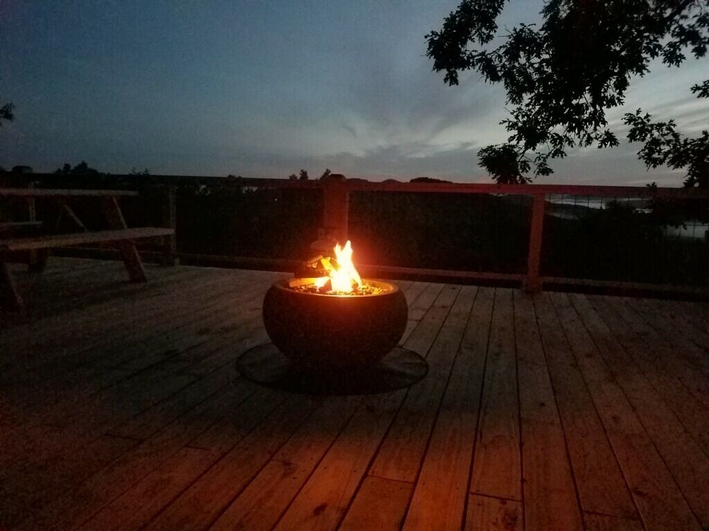 Un pozo de fuego en una terraza de madera con vista a un cuerpo de agua y un árbol al fondo.