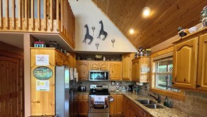 Eine Küche mit Holzausstattung, Granit-Arbeitsplatten, einer Mikrowelle, einem Herd und einem Kühlschrank.