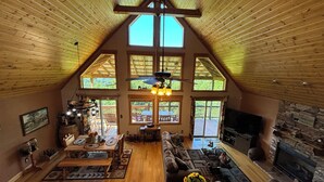 Ein geräumiges Wohnzimmer mit hohen Decken, Holzbalken, einem Kamin und großen Fenstern.