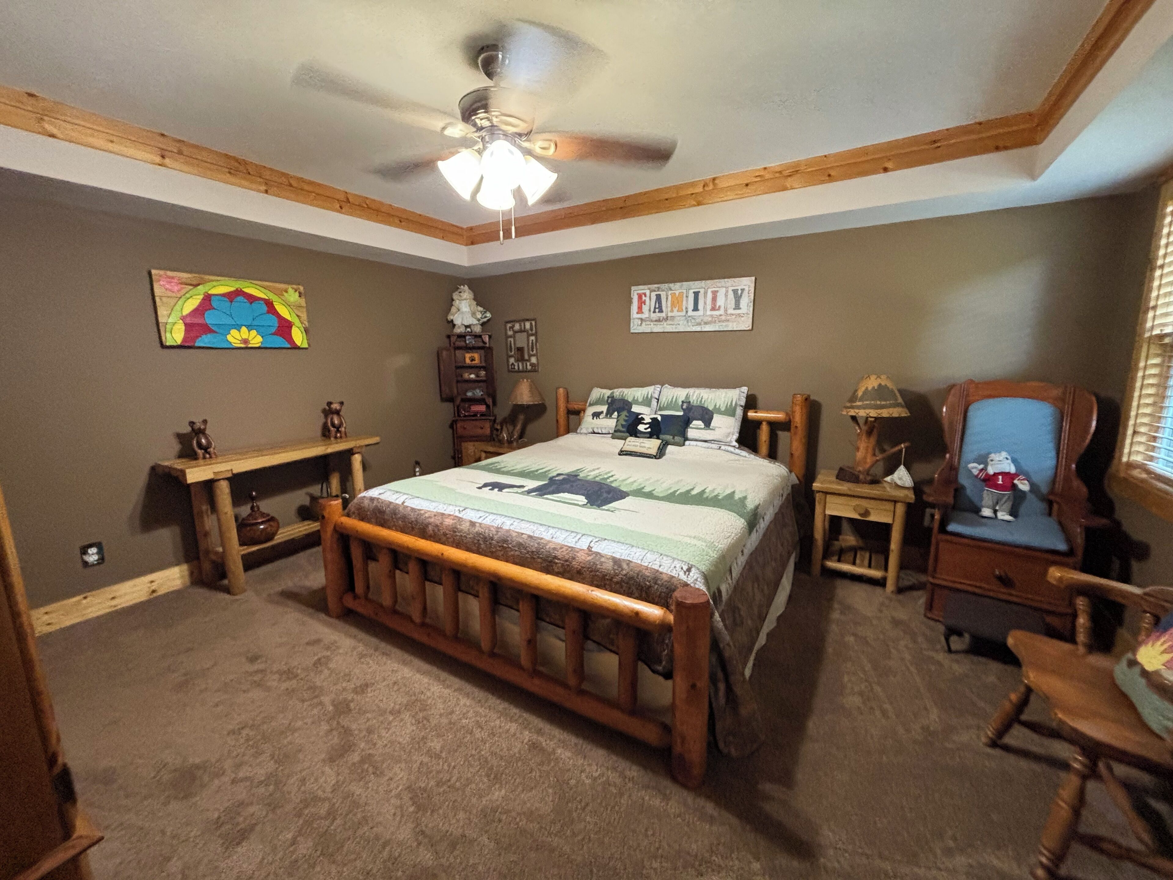 Een slaapkamer met een houten bed, een plafondventilator, een nachtkastje, een stoel en een muur met een 'FAMILY' bord.