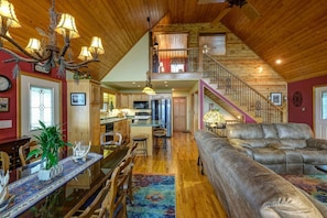 A spacious loft-style living area with a high ceiling, a dining table with chairs, a leather sofa, and a staircase leading to an upper level. - Longview - Captivating views like no other! (Murphy)