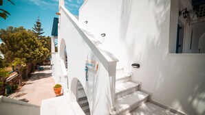 A white building with a staircase leading to a door, surrounded by trees and a clear sky. - Cycladic Seaside House “Eleftheria” in Naxos Island by Kastraki Family House (Kastraki)
