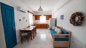 A compact kitchen with wooden cabinets, a dining table, and a sofa. - Cycladic Seaside House “Eleftheria” in Naxos Island by Kastraki Family House (Kastraki)